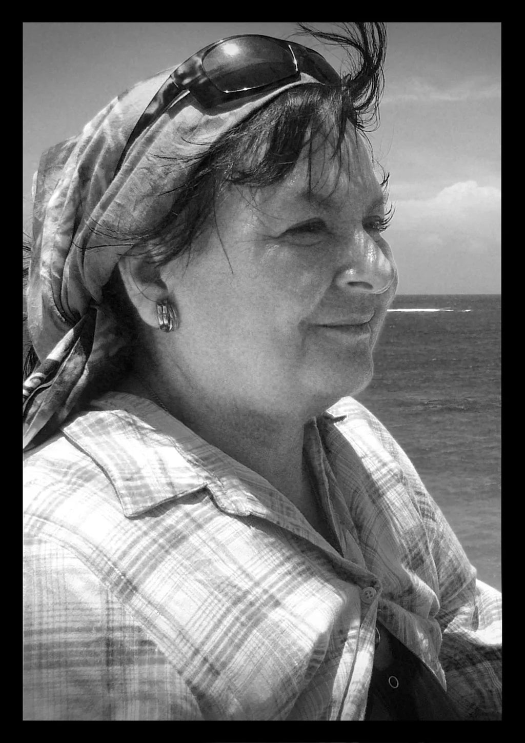 Smiling woman in checkered shirt and headscarf at seaside, black and white portrait